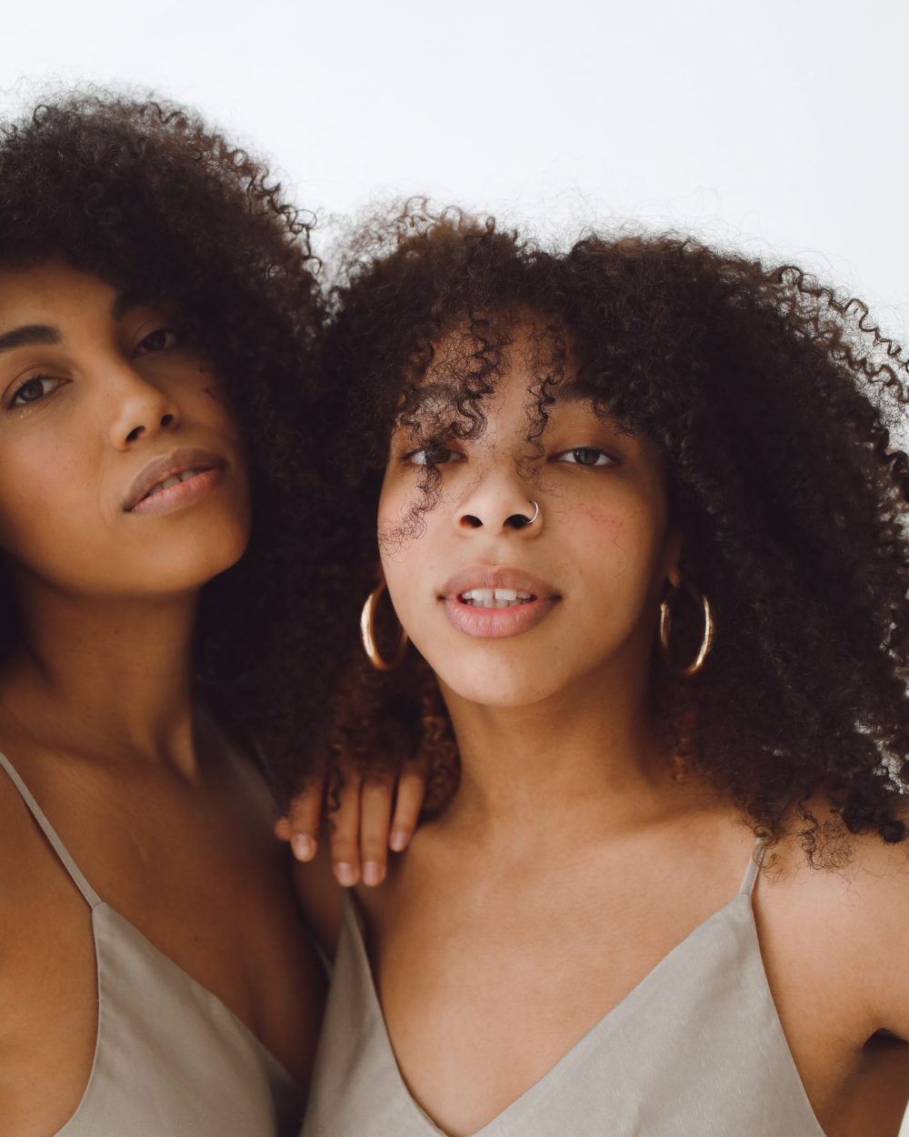 Two women with natural curly hair in soft neutral tones